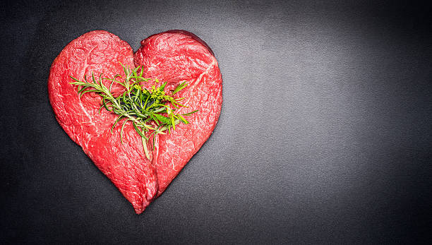 istock Heart shape raw meat with herbs on dark chalkboard background 528578964