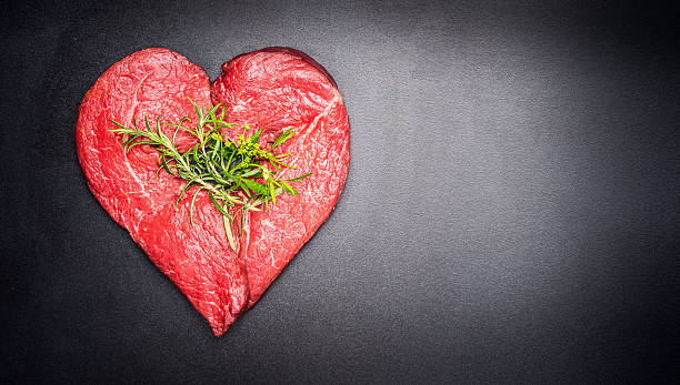 Heart shape raw meat with herbs on dark chalkboard background stock photo