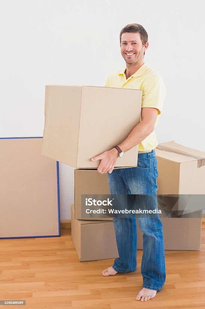 Smiling man carrying cardboard moving boxes at home Smiling man carrying cardboard moving boxes at home in the living room 30-39 Years Stock Photo