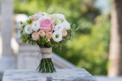 a bridal bouquet of roses, freesia, eustoma standing on a stone background