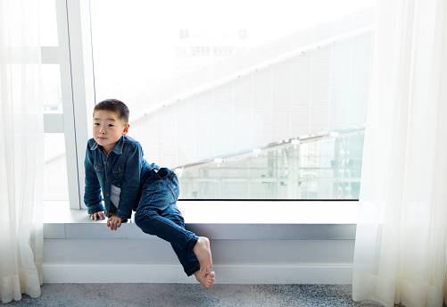 Little asian boy sitting on window sill