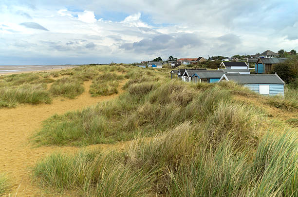 Blue painted beach huts amongst the sand dunes at Old Hunstanton, Norfolk, in Eastern England in early autumn. A few people are on the beach and The Wash can be seen to the left.