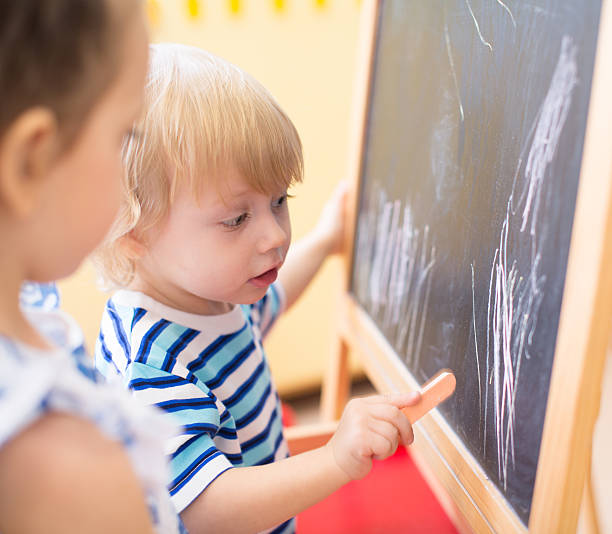 istock Little kids with chalk near blackboard side view 528612186
