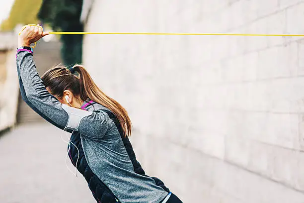 Young woman in sports wear training with elactic band on a wall outdoors, with copy space. Shot made during Istockalypve Paris 2016 event.