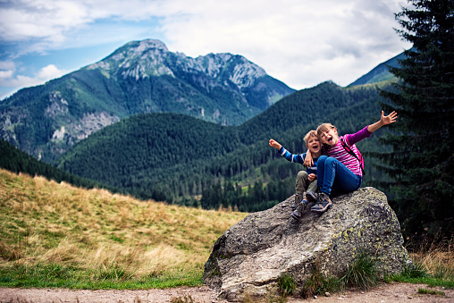 Happy little hikers sitting on big stone laughing and posing to a photo. Tatra mountains visible in background. 