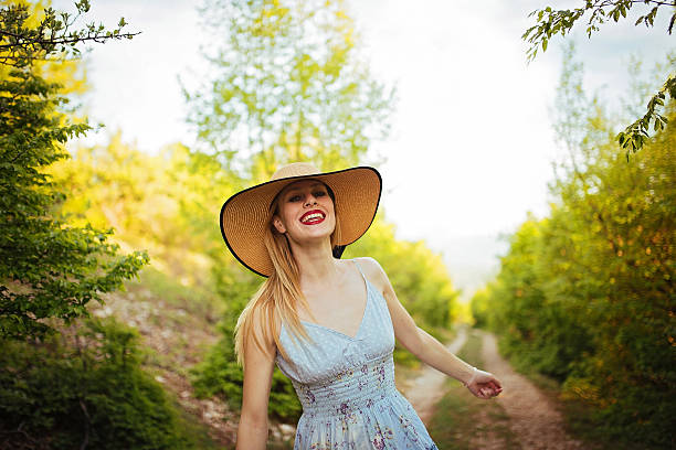 Blonde woman with a hat, laughing in the forest, on a sunny day.