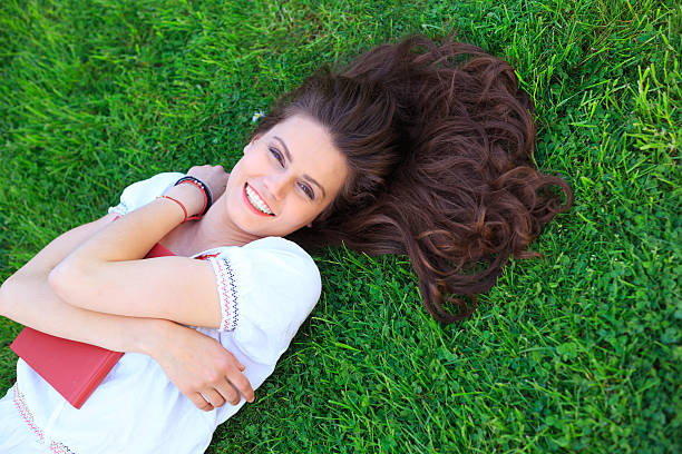 istock Smiling young woman lying on grass and holding a book 528621872