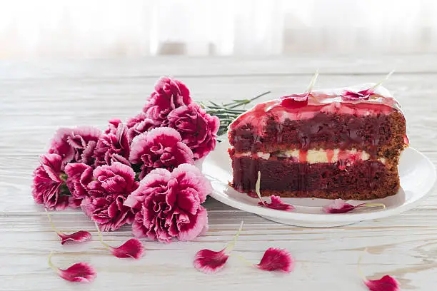 Red velvet cake and pink carnations on wooden table