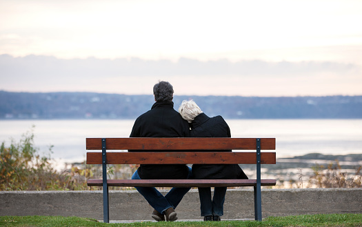 Rear view of mature couple sitting on park bench overlooking river.