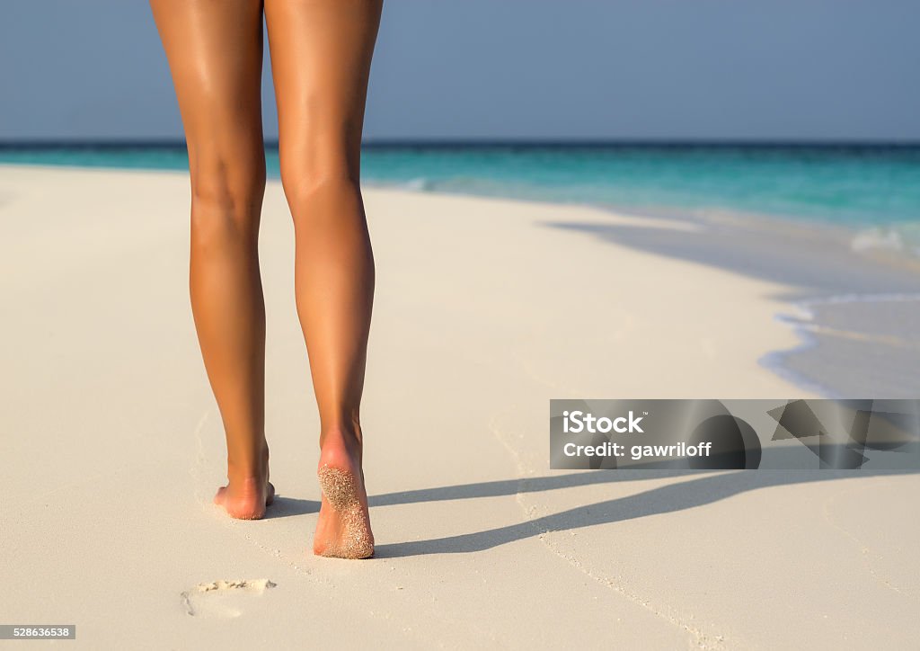 Beach travel - woman walking on sand beach leaving footprints Beach travel - woman walking on sand beach leaving footprints in the sand. Closeup detail of female feet Women Stock Photo