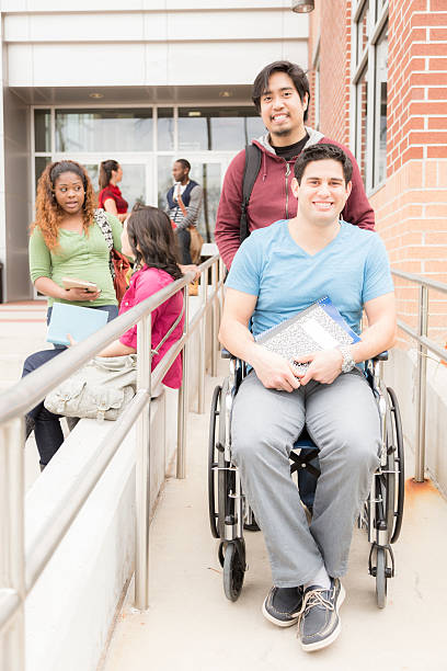 istock Education: Disabled student helped down wheelchair ramp. College campus. 528637224