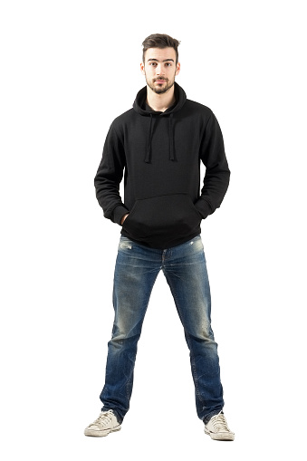 Young confident man in hood with hands in pocket looking at camera. Full body length portrait isolated over white background.