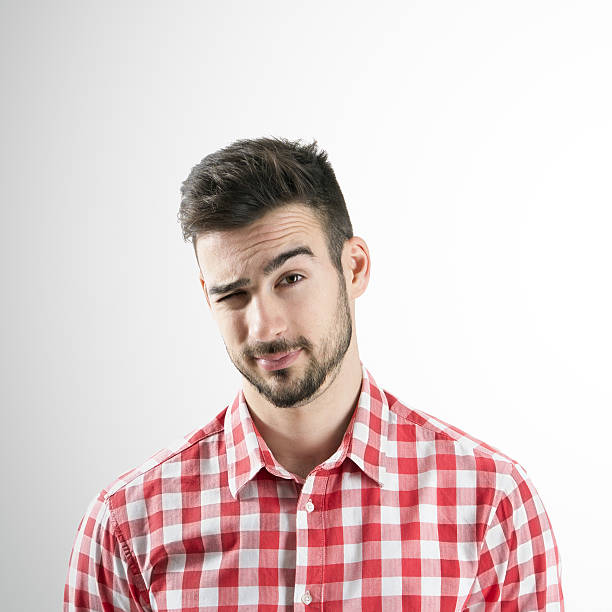 Portrait of young bearded man winking with his right eye Portrait of young bearded man winking with his right eye over gray background. young man wink stock pictures, royalty-free photos & images
