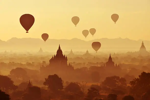 Hot air balloons fly over the ancient pagodas of Bagan in semi silhouette at dawn