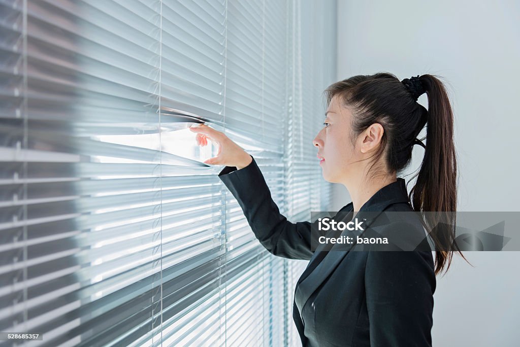 curiosity Young beautiful businesswoman looking out of the window through the blinds 30-39 Years Stock Photo