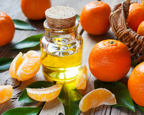 Bottle of essential citrus oil and ripe tangerines with leaves on old wooden kitchen table.