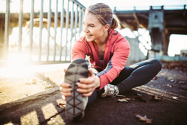 Athlete Stretching at Portland Waterfront A young athletic woman stretches out her legs before going on a morning jog, running the paths at Tom McCall Waterfront Park in Portland, Oregon. The sun shines from behind the Burnside bridge, giving a warm glow to the image. early fall stock pictures, royalty-free photos & images