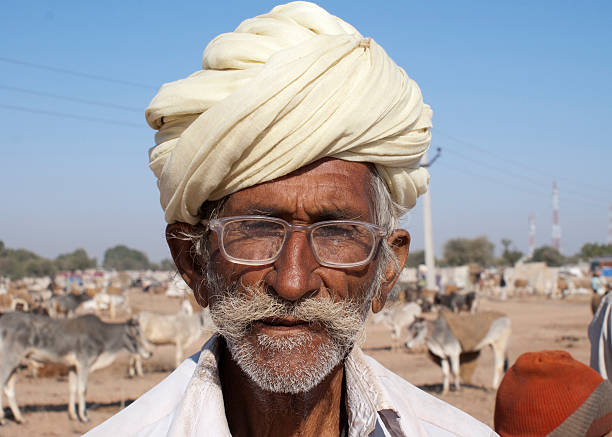 Nagaur, India - February 10, 2011: Old cattle farmer wears white turban. gray mustache and glasses, covered with dirt.