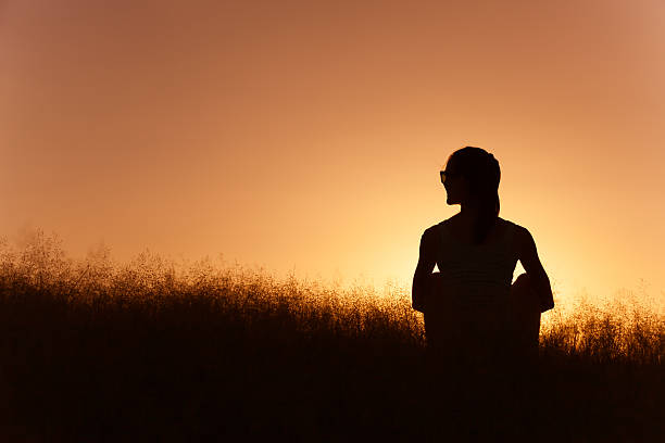 giovane ragazza seduta in un campo d’erba. - shadow focus on shadow women sunset foto e immagini stock