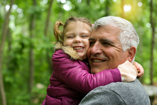 Happy kid hugging grandfather in the park.