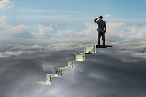 businessman on top of money stairs looking at natural sky cloudscape background