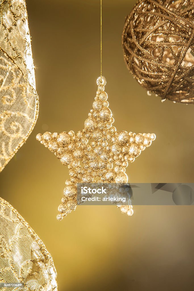 Golden Christmas star Small gold Christmas star hanging on a golden thread with golden background and bright flashes . Christmas decoration item . Christmas Stock Photo