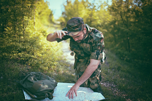 Soldier in the forest looking at his map, tries to find the right strategy.