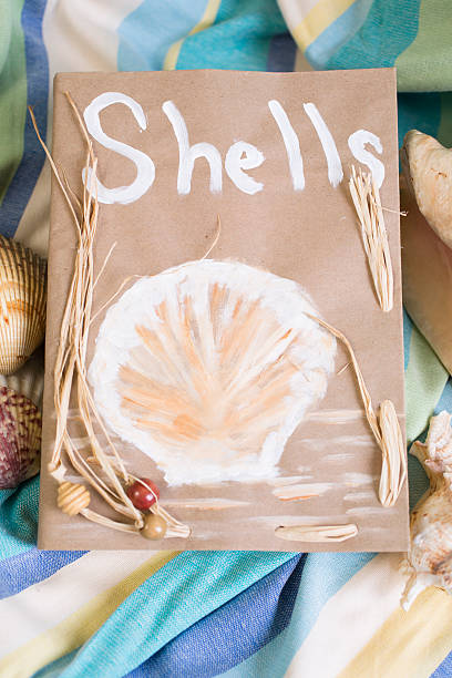 Summer vacation.  Paper bag filled with seashells on beach blanket.
