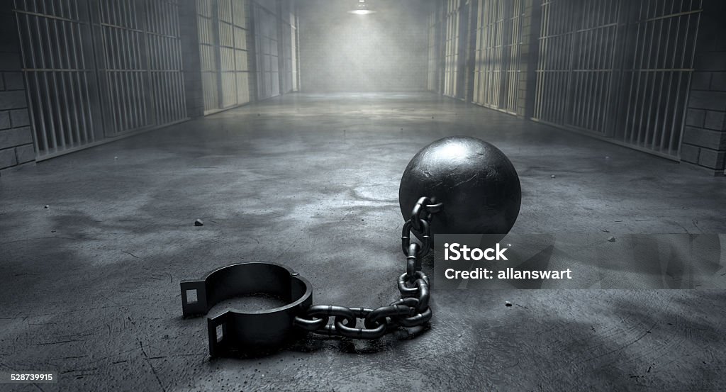 Ball And Chain In Prison A vintage ball and chain with an open shackle on an old prison cell block floor lit by overhead lights Ball and Chain Stock Photo