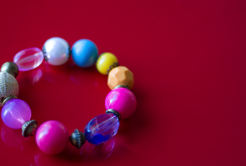 A close-up shot of a colorful beaded bracelet on a red background. Copy space available.