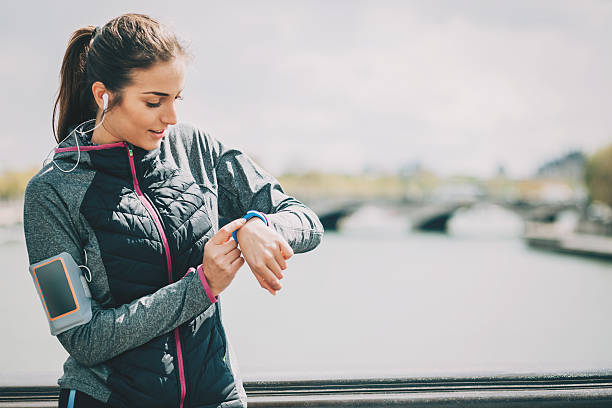 Sports woman checking her tech watch Sports woman with headphones having a rest and looking at her smart watch outdoors in Paris. pedometer photos stock pictures, royalty-free photos & images
