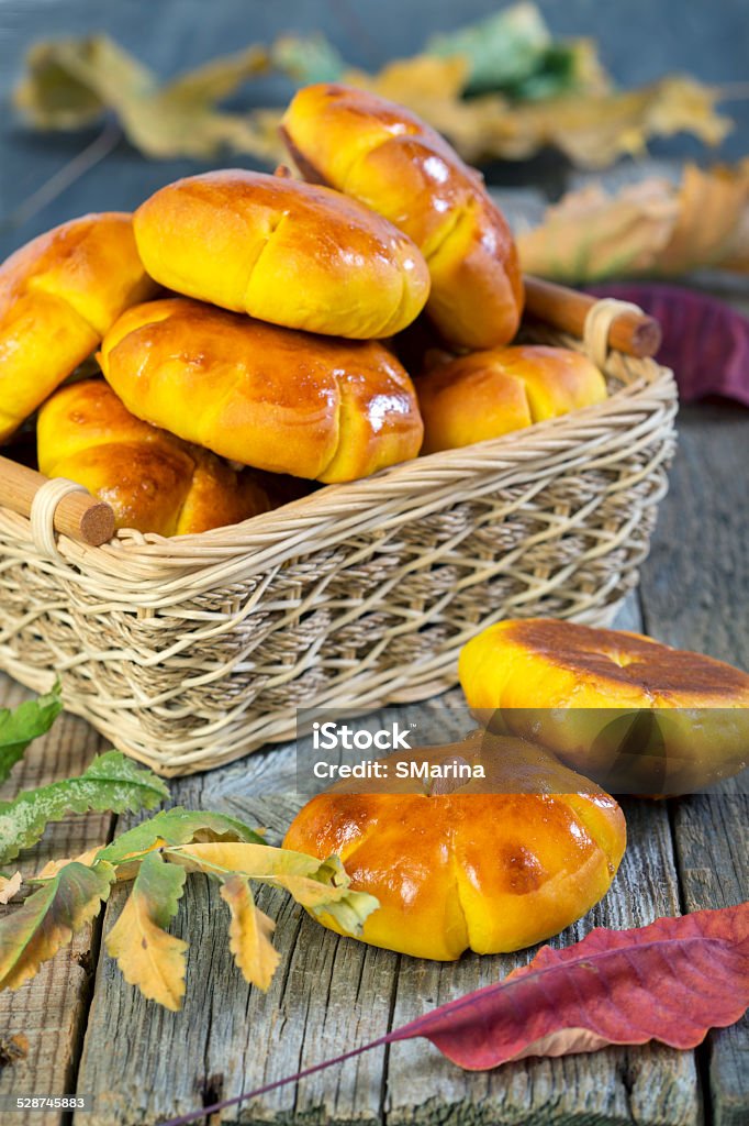 Pumpkin buns in a wicker basket. Basket with buns and autumn leaves on an old table. Autumn Stock Photo