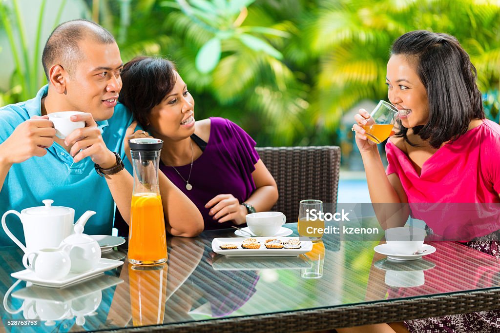 Asian friends having coffee on home porch Asian friends having coffee on the porch in front of a home, in the background a tropical garden Adult Stock Photo