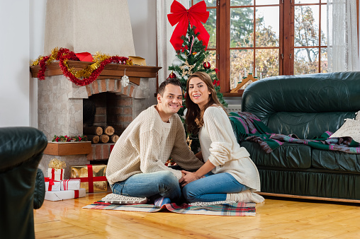 Celebrating Christmas together. Beautiful young couple sitting on the floor in christmas decorated living room  and smiling