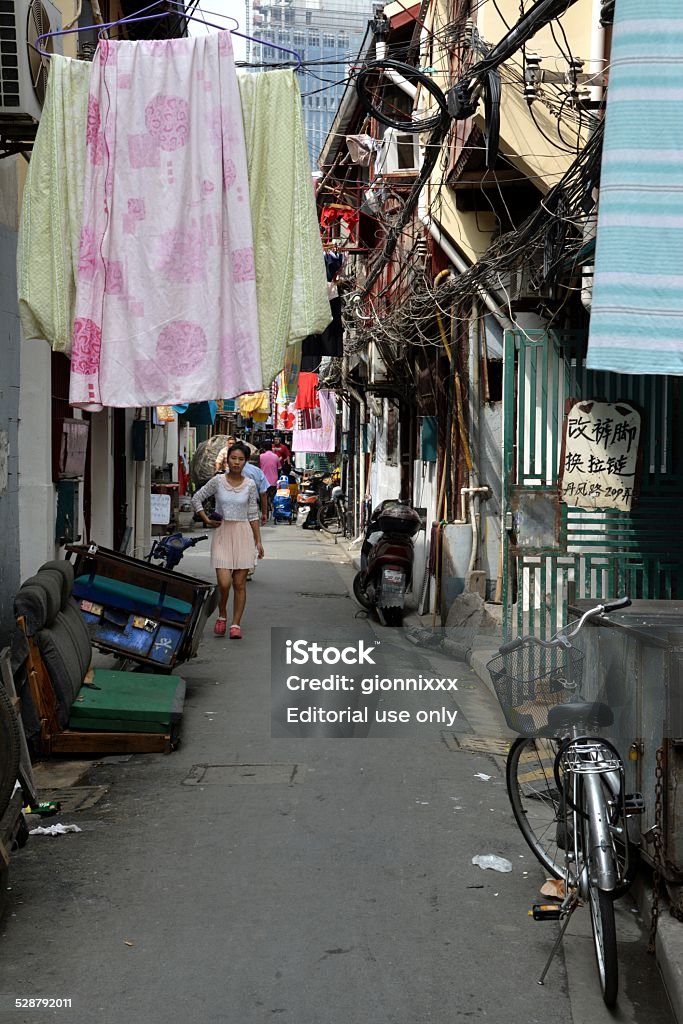 Shanghai Old town, Shikumen street scene Shanghai, China - September 20, 2014: Girl in the background walking on a narrow street in Shanghai old town, surrounded by cables, hanging drying clothes and sheets. Bicycle Stock Photo