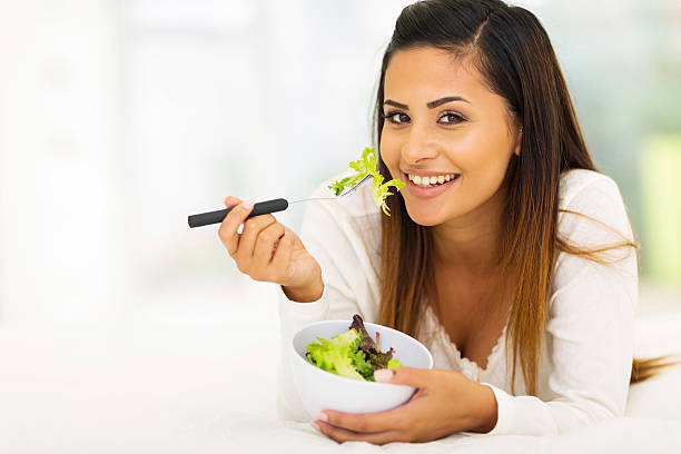 istock gorgeous woman lying on bed eating vegetable salad 528828095