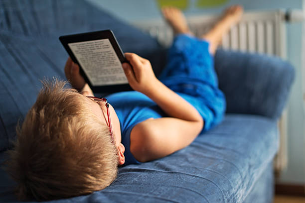 Little boy reading an ebook on couch Little boy lying on the couch, reading a ebook. e reader photos stock pictures, royalty-free photos & images