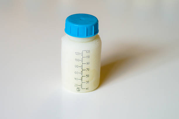 Pink babies bottle half full of milk on white