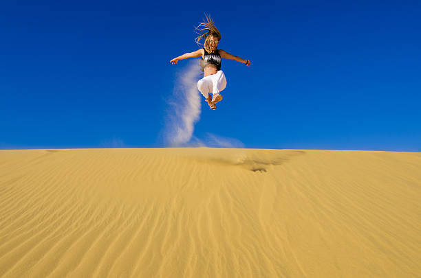 istock girl jumping on the yellow sand dune 528864195