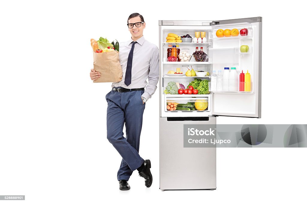 Man holding grocery bag and leaning on a fridge Man holding a grocery bag and leaning on a fridge isolated on white background 20-29 Years Stock Photo