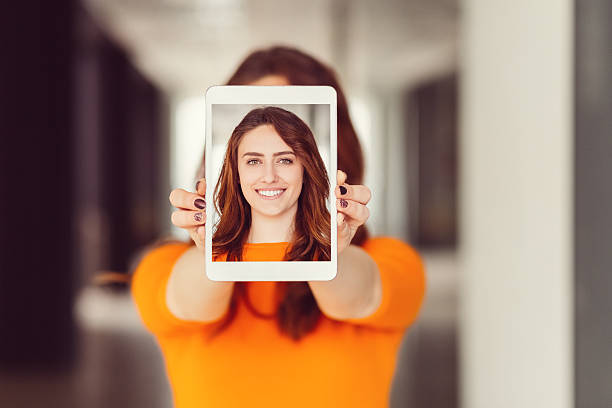 Young woman showing self portrait on tablet pc Smiling girl showing selfie on tablet in front of photos stock pictures, royalty-free photos & images