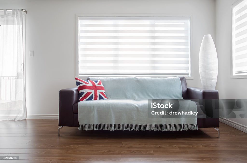 Modern Sofa in bright living room with zebra blinds. Horizontal image of  a modern leather sofa with throw and a Union Jack pillow, in bright living room. Space for copy. Window Blinds Stock Photo