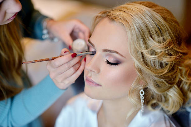 Wedding makeup artist making a make up for bride Wedding makeup artist making a make up for bride. Beautiful sexy model girl indoors. Beauty woman with curly hair. Female portrait. Bridal morning of a cute lady. Close-up hands near face getting dressed stock pictures, royalty-free photos & images