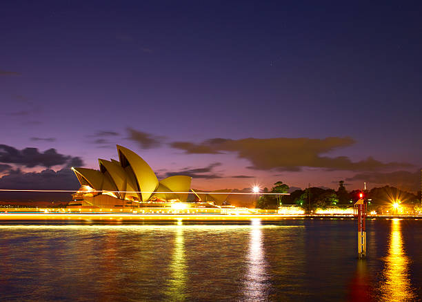 Sydney Australia - April 1, 2016: Early morning in Sydney, and light trails from a ferry steam past the iconic shape of the city's Opera House. Beyond can be seen a glorious pre-dawn sky .