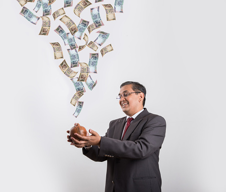 indian businessman catching flying currency in his piggy bank made up or clay, happy asian businessman with piggy bank under falling indian currency notes