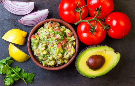 Guacamole and ingredients - avocado, tomatoes, onion, cilantro dark background.