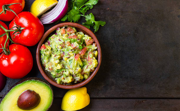 guacamole i składniki-awokado, pomidory, cebula, liście kolendry ciemnym tle. - avocado lemon snack cracker zdjęcia i obrazy z banku zdjęć