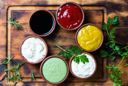 Sauces ketchup, mustar, mayonnaise, wasabi, soy sauce in clay bowls on wooden cutting board