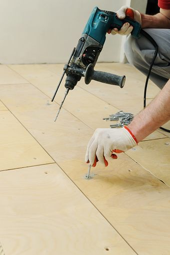 Laying plywood on the floor. Worker inserts the dowel to fix a plywood.