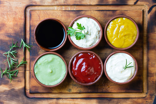 Sauces ketchup, mustar, mayonnaise, wasabi, soy sauce in clay bowls on wooden cutting board
